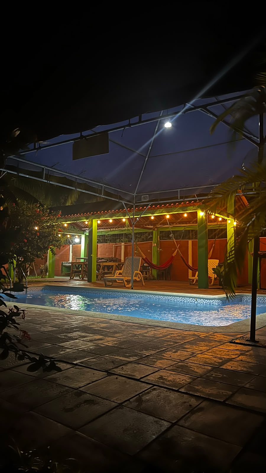 Hamaquero con luces colgantes, hamacas y mesas junto a la piscina de noche