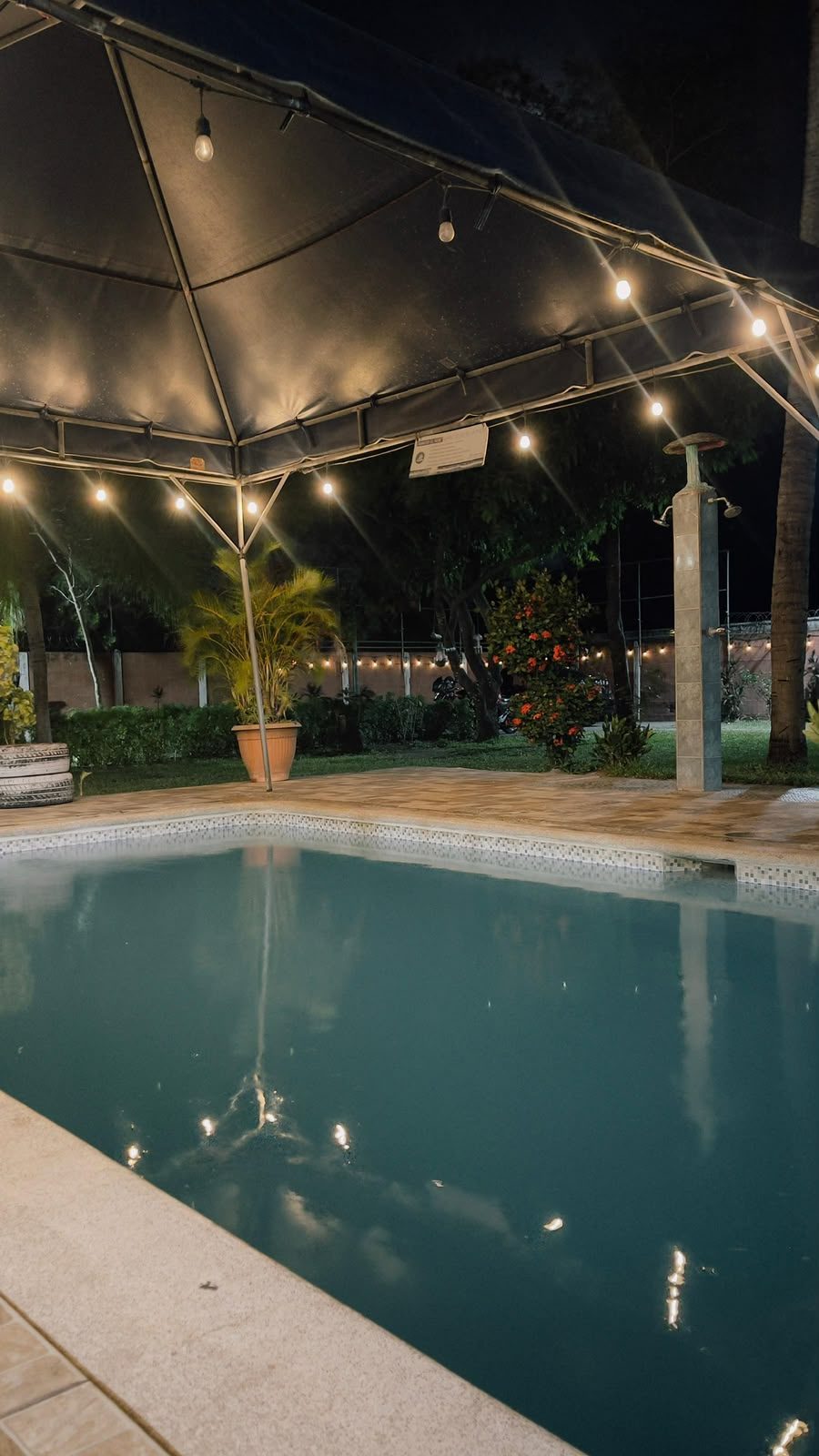 Piscina de noche con reflejos de luces colgantes bajo el toldo